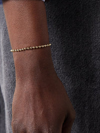 Gold beaded bracelet on a wrist against a dark textured background