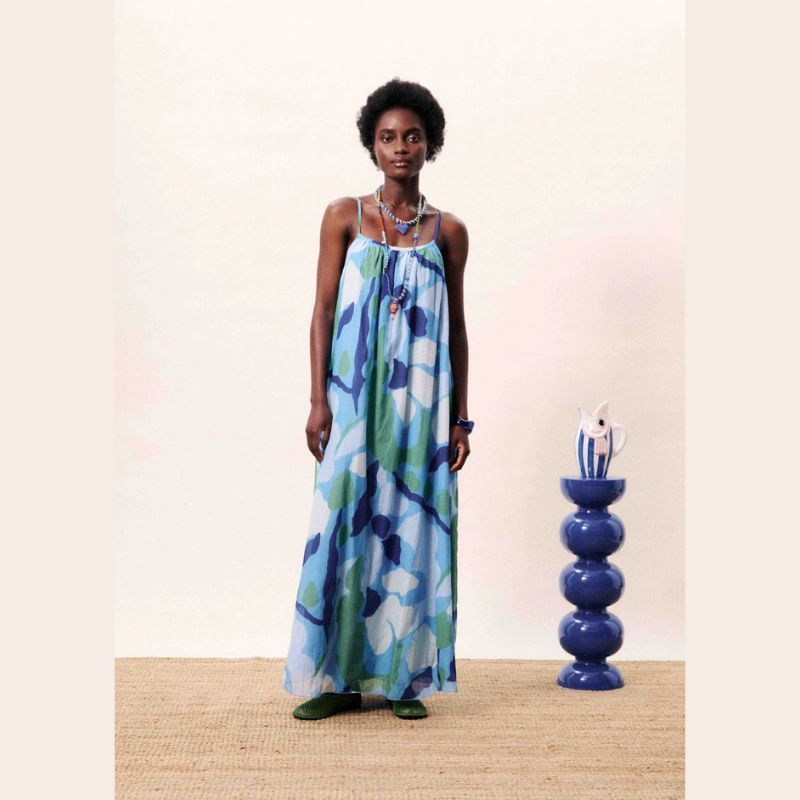 Woman wearing a floral dress standing next to a blue vase on a beige surface.