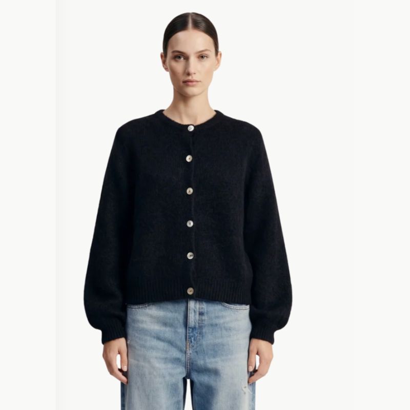 A black soft Alpaca wool cardigan has a crewneck and long sleeves and is paired with jeans on the model. 