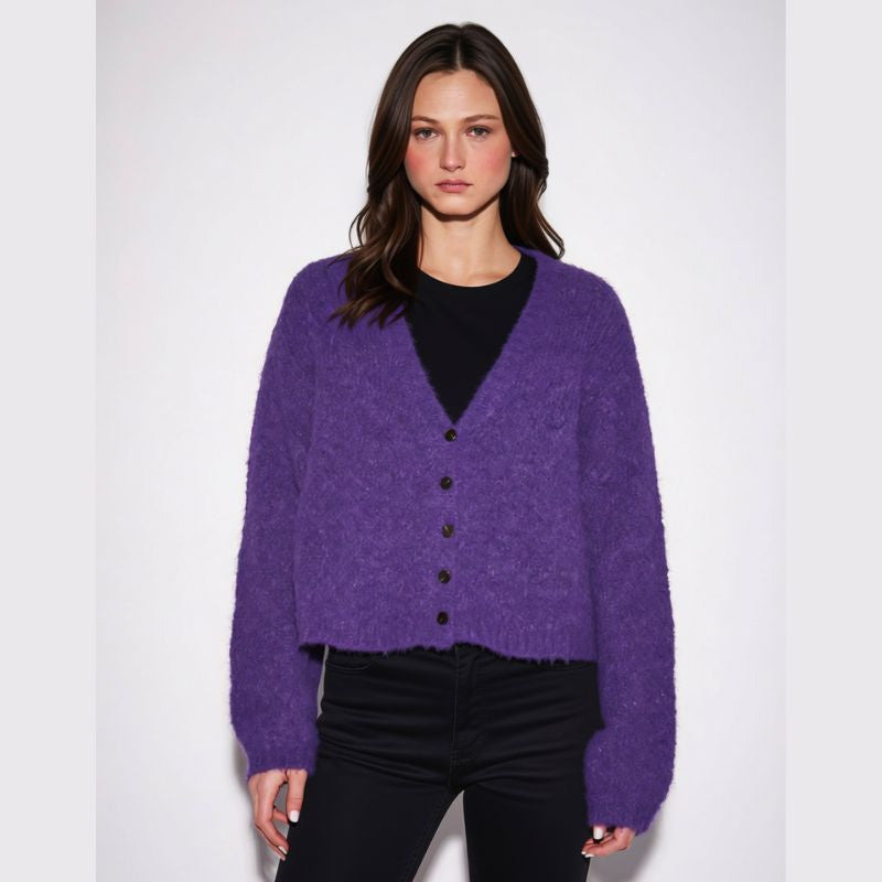 A woman modeling a purple fuzzy button-front cardigan over a black top and black pants, photographed against a plain light gray studio background.