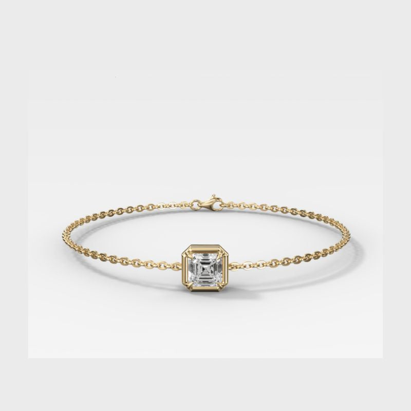 A delicate gold chain bracelet featuring a central square bezel-set diamond, displayed on a clean light gray background.
