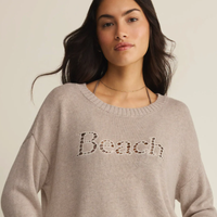 Woman wearing a beige sweater with 'Beach' text