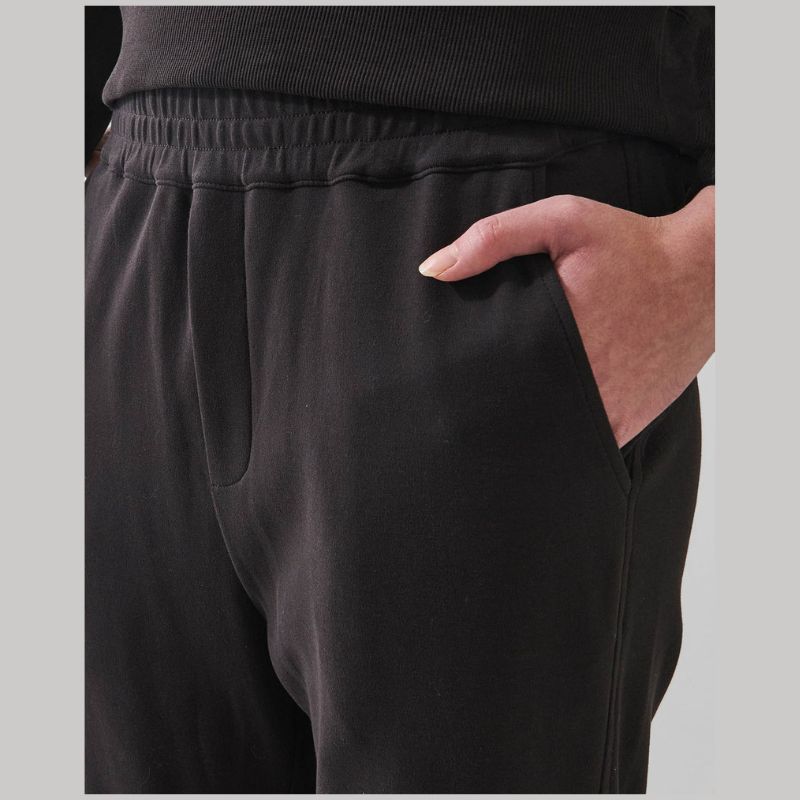 Close-up of a person wearing black sweatpants with an elastic waistband and side pocket, showing a hand in the pocket.