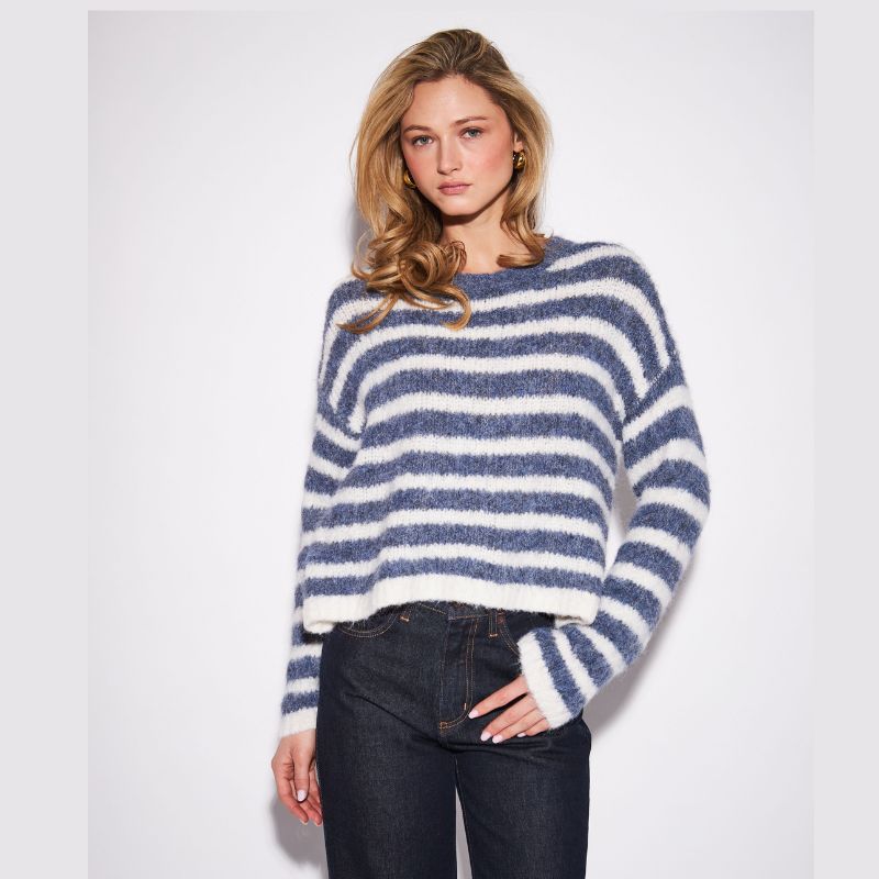 A woman modeling a fuzzy, cropped knit sweater with horizontal navy blue and off-white stripes, paired with dark wash jeans, against a plain light gray studio background.