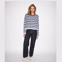 A woman modeling a fuzzy, long-sleeve crewneck sweater with horizontal navy and white stripes, paired with dark wash jeans and white flat shoes, against a light gray studio background.