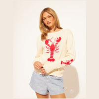 Woman wearing a cream sweater with a red lobster design and striped shorts on a white background