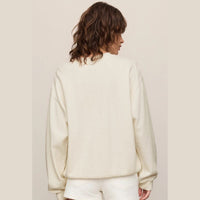 A woman shown from the back wearing a cream-colored crewneck sweatshirt and matching white shorts against a solid light beige background.