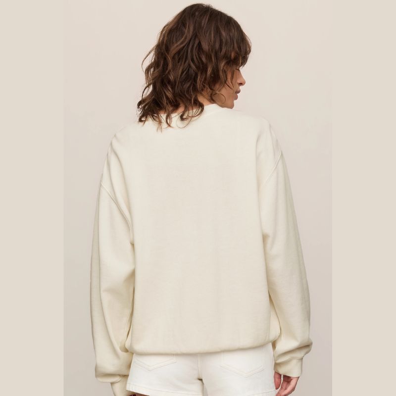 A woman shown from the back wearing a cream-colored crewneck sweatshirt and matching white shorts against a solid light beige background.