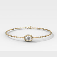 A delicate yellow gold chain bracelet with a central bezel-set cushion-cut diamond, photographed on a clean light gray background.