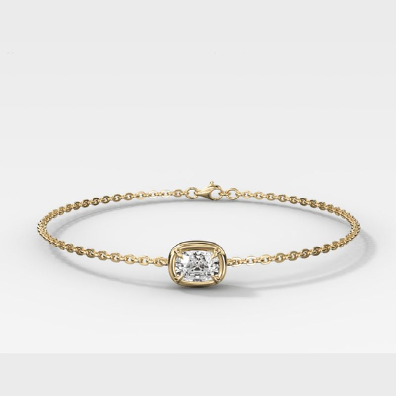 A delicate yellow gold chain bracelet with a central bezel-set cushion-cut diamond, photographed on a clean light gray background.