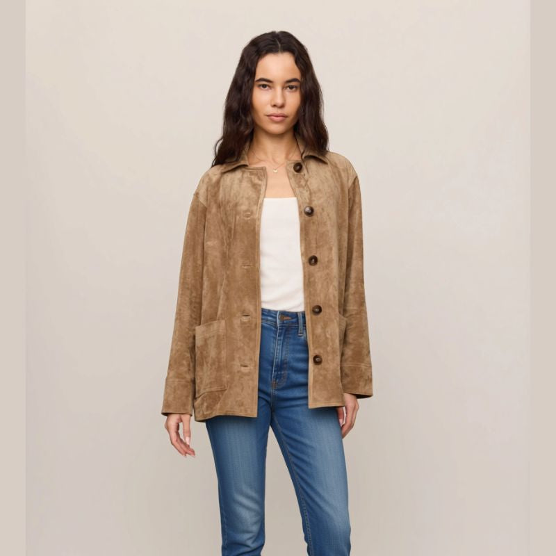 A woman modeling a tan suede-like button-front jacket over a white top and blue jeans, standing against a plain light beige studio background.