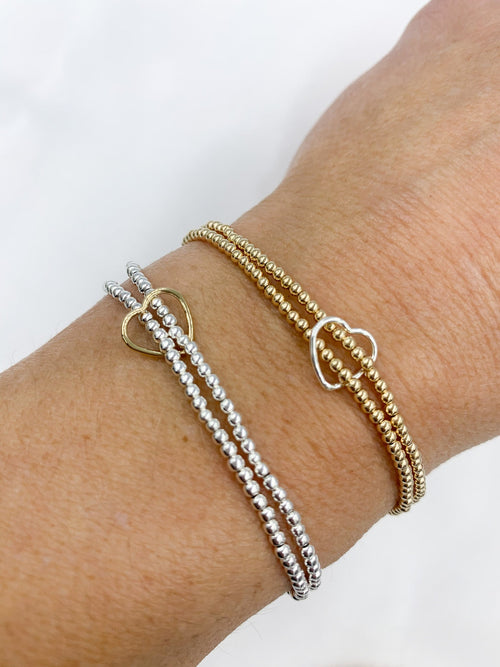 Showcasing the double strand 2mm bead bracelet  held together with a heart charm. model is  wearing both  the Sterling Silver and the Gold fil options.  