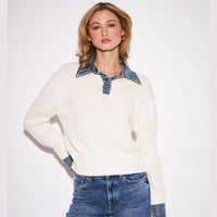 A woman modeling a cream knit sweater with a denim collar and matching denim cuffs, paired with blue jeans, against a plain white studio background.