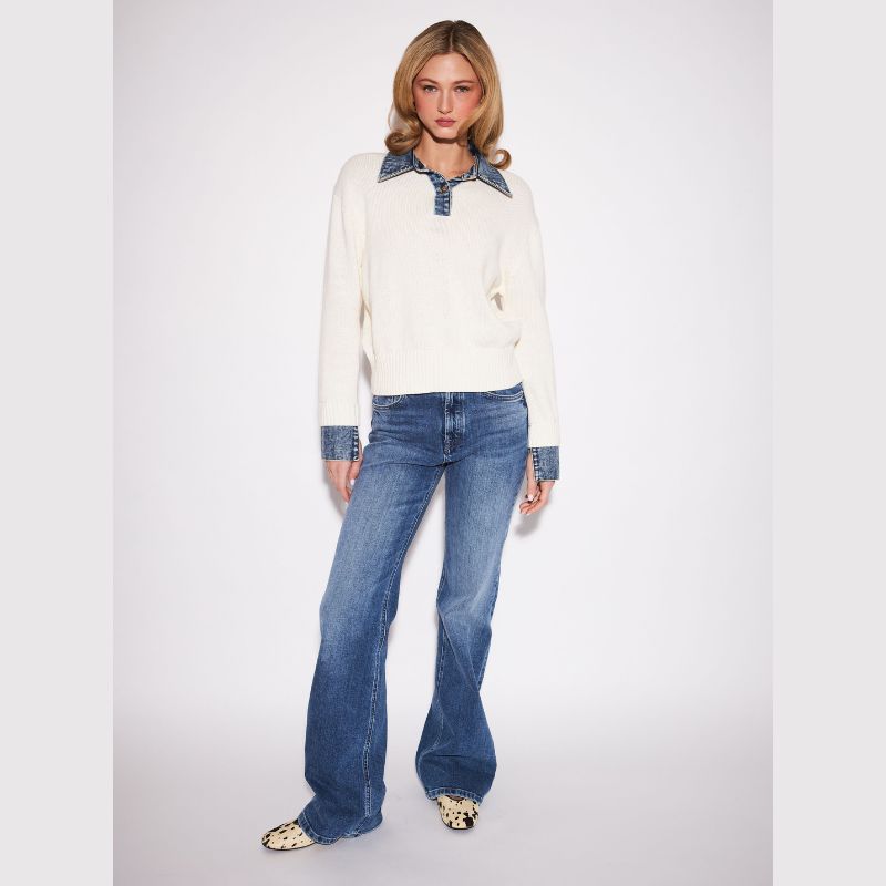 A model stands against a light gray studio background wearing a cream knit sweater with a blue denim collar and cuffs, blue jeans, and leopard-print shoes.