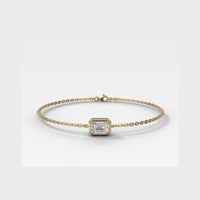 A delicate yellow gold chain bracelet featuring a central bezel-set rectangular clear gemstone, displayed on a clean light gray background.
