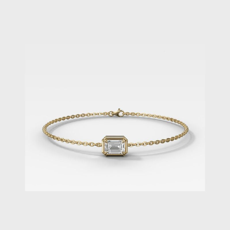 A delicate yellow gold chain bracelet featuring a central bezel-set rectangular clear gemstone, displayed on a clean light gray background.