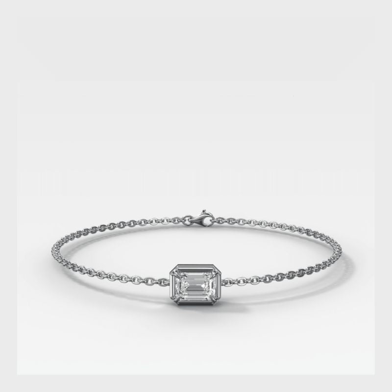 A delicate white Gold chain bracelet featuring a central rectangular emerald-cut clear gemstone in a prong setting, displayed on a clean light gray background.