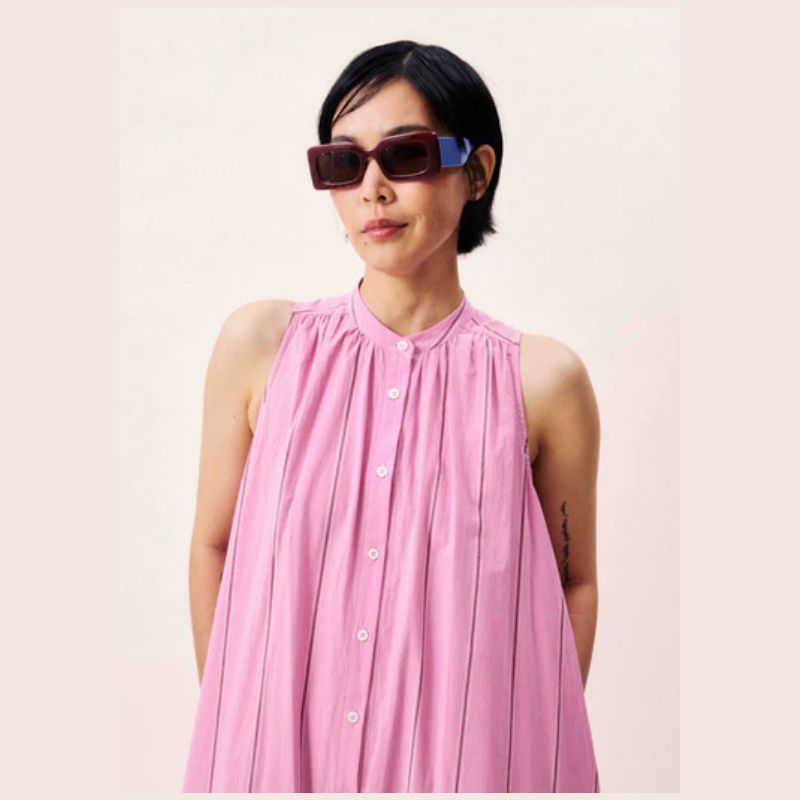 Woman wearing a pink pinstriped sleeveless dress with mother of pearl buttons a the front. 
