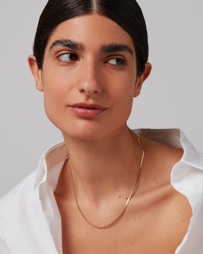 Woman wearing a gold necklace against a neutral background