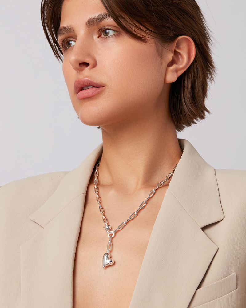 Woman wearing a necklace with a heart pendant against a neutral background