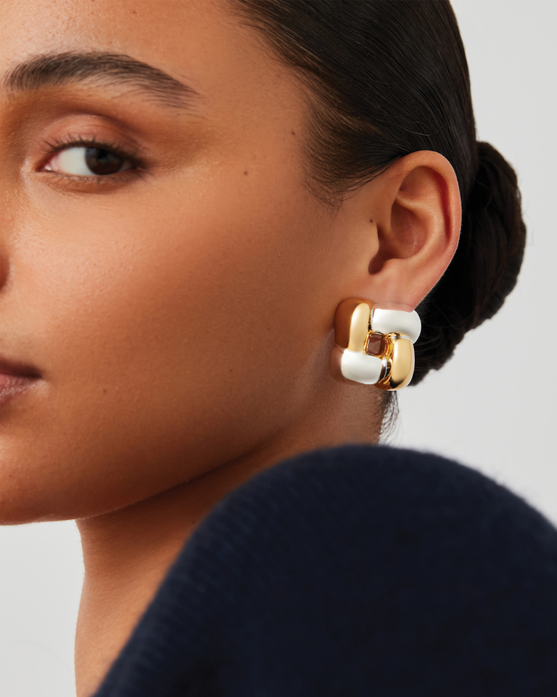 Close-up of a person wearing gold and silver earrings against a neutral background