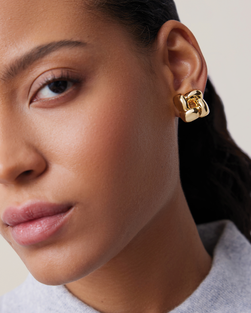 Close-up of a person wearing a gold hoop earring against a neutral background