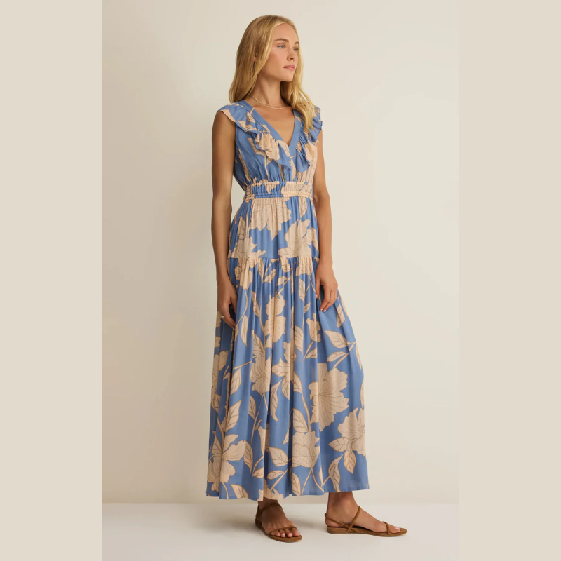 Woman wearing a V- neck blue and beige floral maxi dress against a plain background