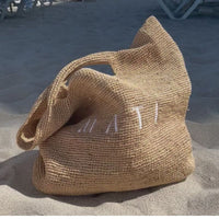Woven bag with 'Matti' embroidery on a sandy surface