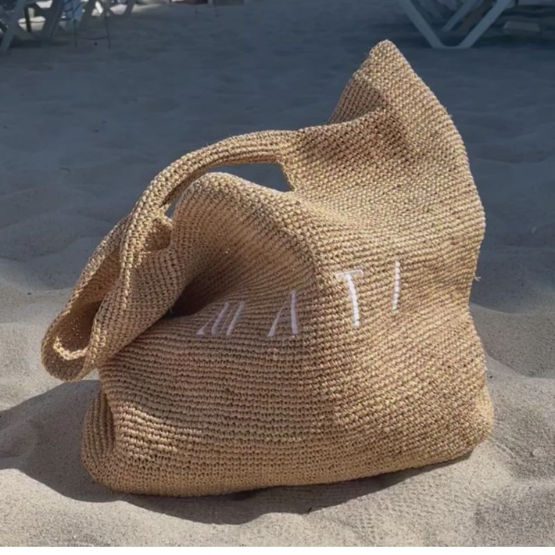 Woven bag with 'Matti' embroidery on a sandy surface
