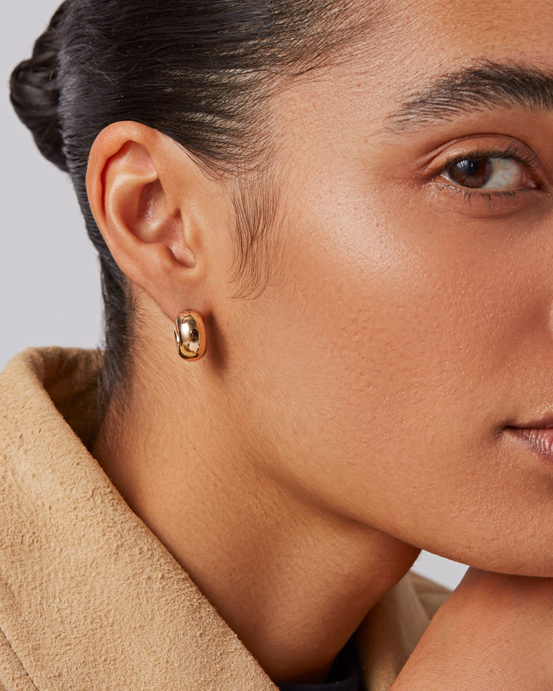 Close-up of a person wearing gold earrings with a neutral background