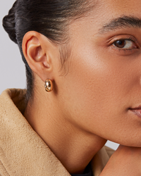 Close-up of a person wearing gold earrings with a neutral background