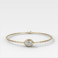 A delicate yellow gold chain bracelet with a single bezel-set Oval lab diamond (horizontal) at the center, displayed on a clean white background.