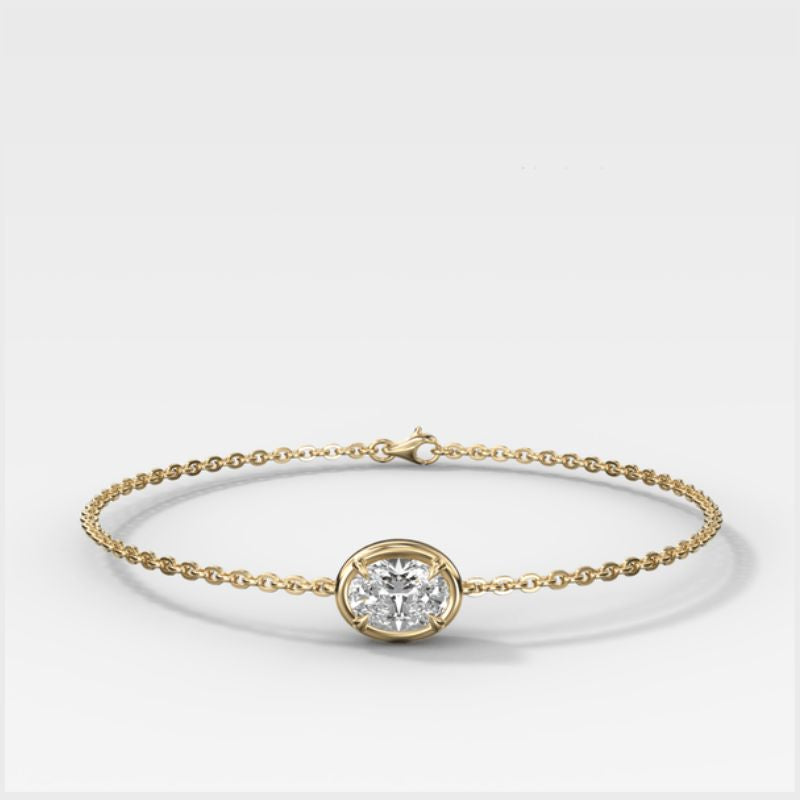 A delicate yellow gold chain bracelet with a single bezel-set Oval lab diamond (horizontal) at the center, displayed on a clean white background.