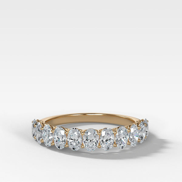 A yellow gold eternity ring featuring a row of oval-cut clear diamonds, set against a clean white background with a soft shadow.