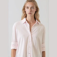 A woman wearing a light pink long-sleeve button-up shirt with rolled-up sleeves, shown from the waist up against a plain light gray background.