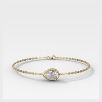 A delicate yellow gold chain bracelet with a small teardrop-shaped bezel holding a clear round gemstone, displayed on a clean white background.