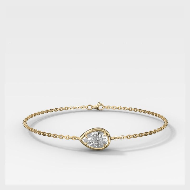 A delicate yellow gold chain bracelet with a small teardrop-shaped bezel holding a clear round gemstone, displayed on a clean white background.