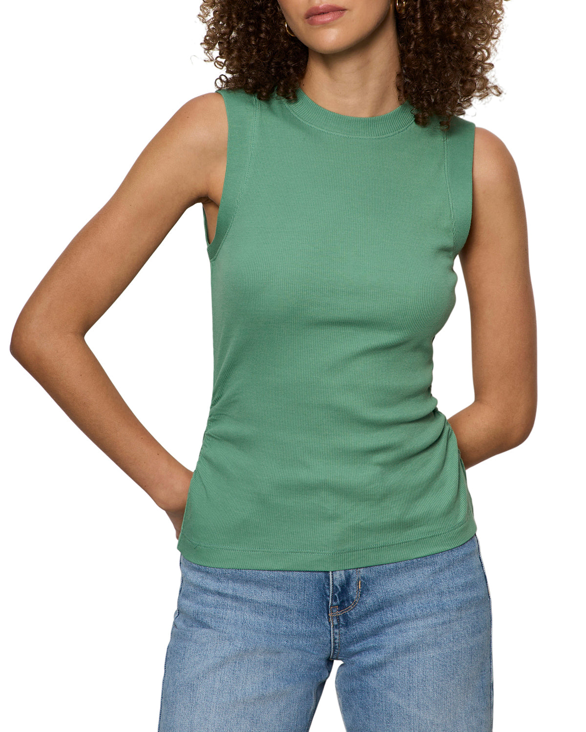 Woman wearing a green sleeveless top and blue jeans on a white background