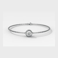 A delicate white gold chain bracelet featuring a central bezel-set round diamond, photographed on a clean light gray background.