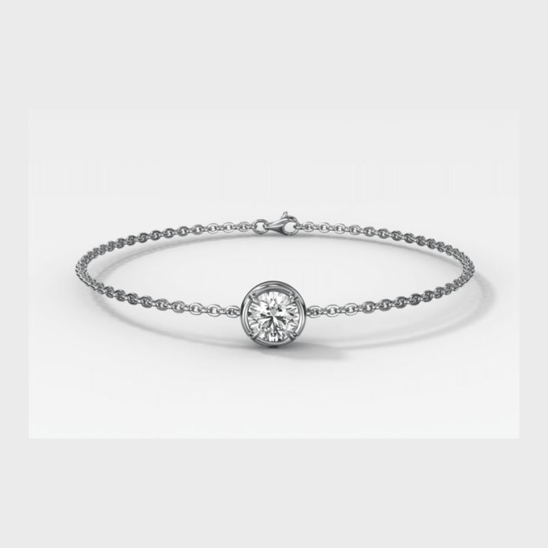A delicate white gold chain bracelet featuring a central bezel-set round diamond, photographed on a clean light gray background.