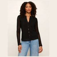 A woman modeling a black long-sleeve button-front top with sheer mesh sleeves, paired with light blue jeans, against a plain light beige studio background.