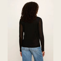 A woman viewed from behind wearing a black long-sleeve mesh top and light blue jeans, standing against a plain off-white background.