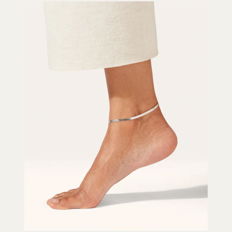 Silver snake chain anklet on a foot with a white background