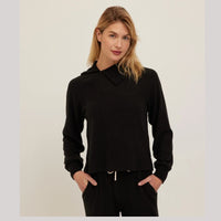 A woman modeling a black long-sleeve cropped hoodie with a mock neck and drawstring, paired with black pants, against a plain light background.