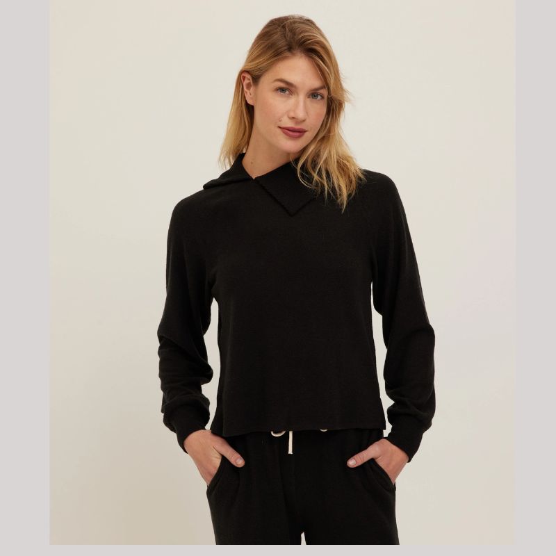 A woman modeling a black long-sleeve cropped hoodie with a mock neck and drawstring, paired with black pants, against a plain light background.