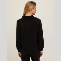 A woman viewed from the back wearing a black long-sleeve mock neck top and black pants against a light gray studio background.