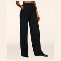 A model wearing black wide-leg trousers with side pockets, paired with black pointed flats, shown from the waist down against a light beige background.