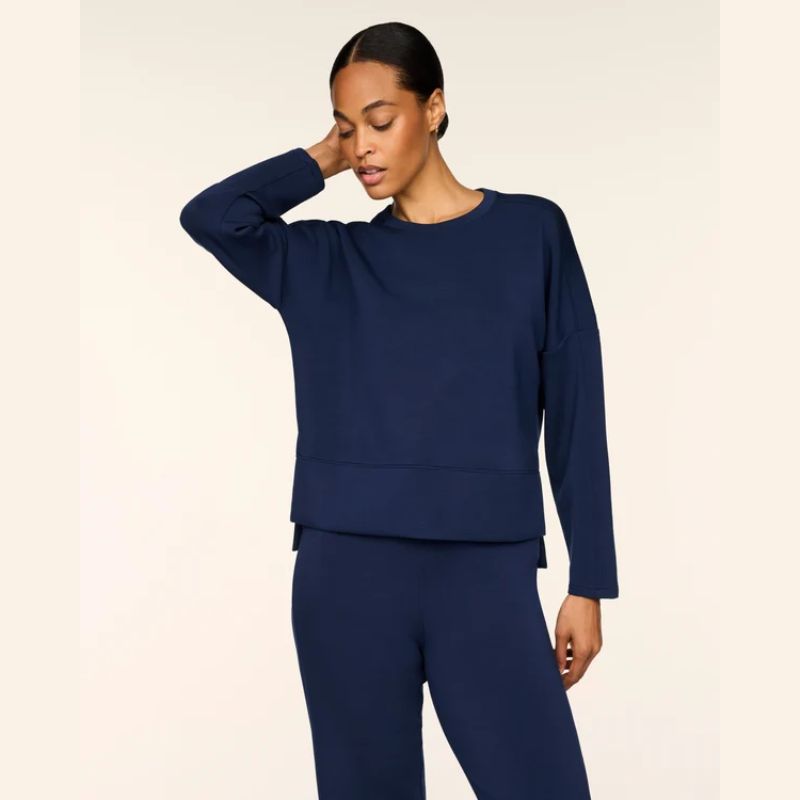 A woman modeling a matching navy blue lounge set consisting of a long-sleeve cropped sweatshirt and high-waisted leggings, set against a plain light beige background.
