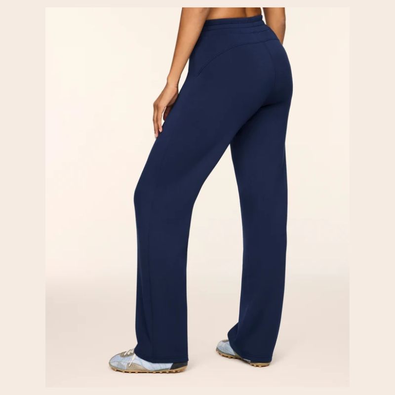 A person wearing navy blue high-waisted, wide-leg pants, shown from a rear three-quarter angle against a plain light beige studio background.