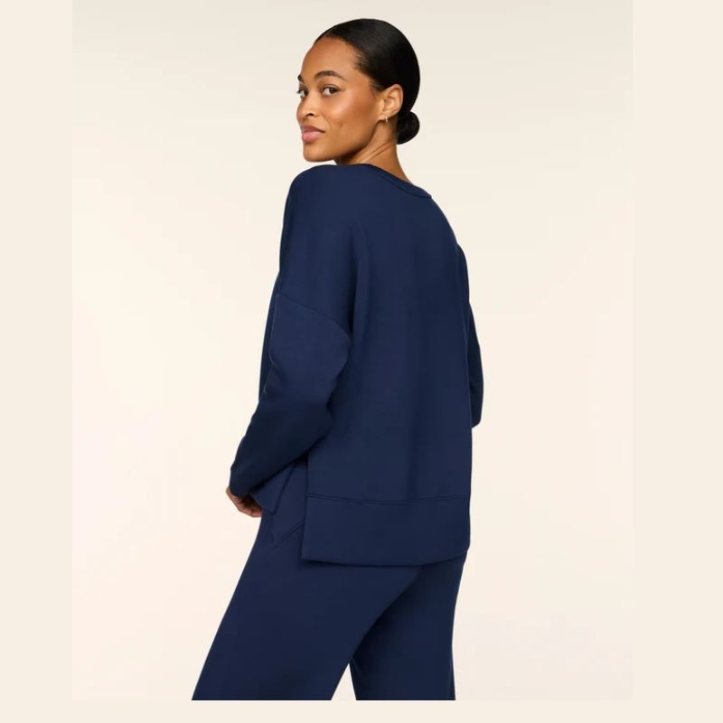 A woman wearing a navy blue knit lounge set, shown from a side-back angle against a solid off-white background.